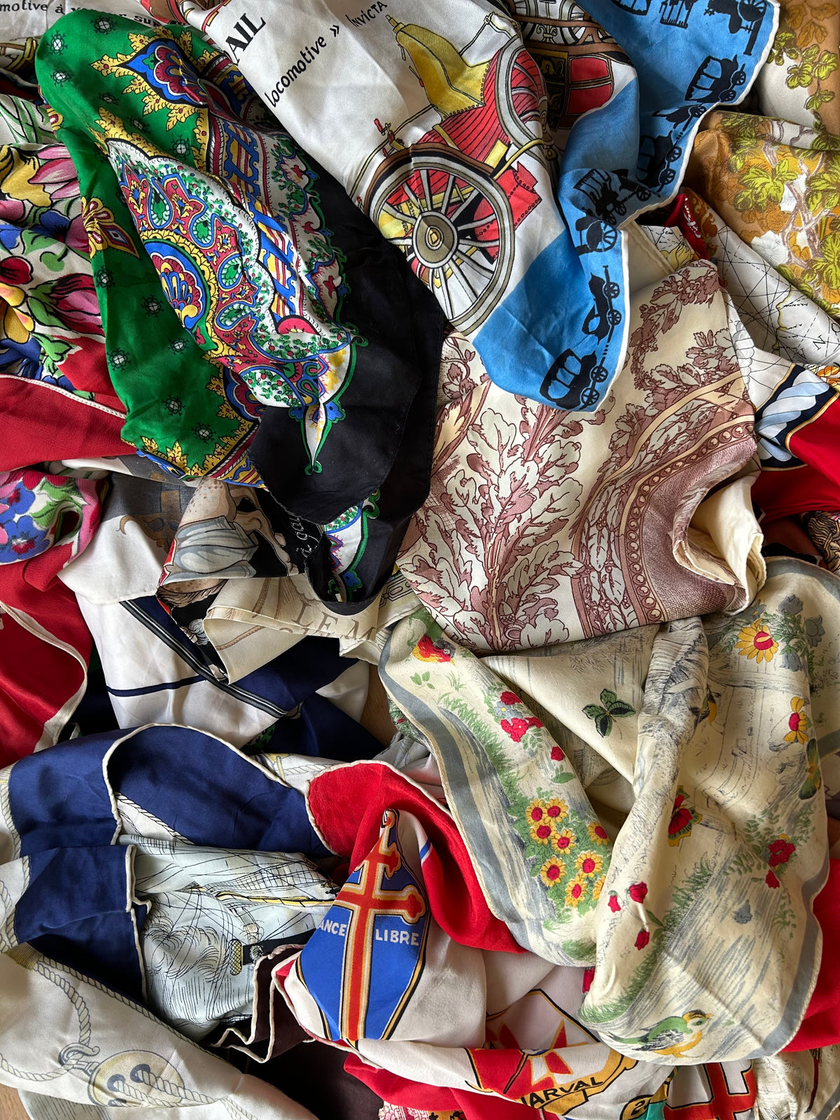 A heap of vintage French printed silk scarves: florals, paisley, carriages, a toile and a Free France crest, with hand-rolled edges
