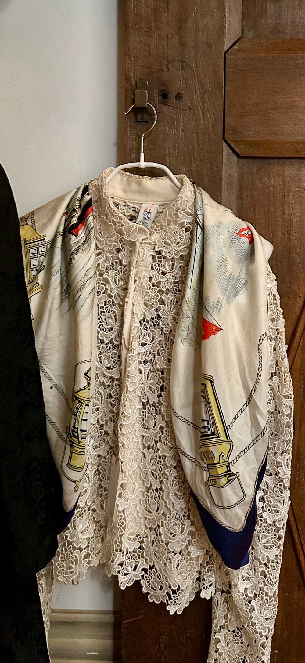 A cream lace blouse with a printed silk scarf over the shoulders, hanging on an old wooden door