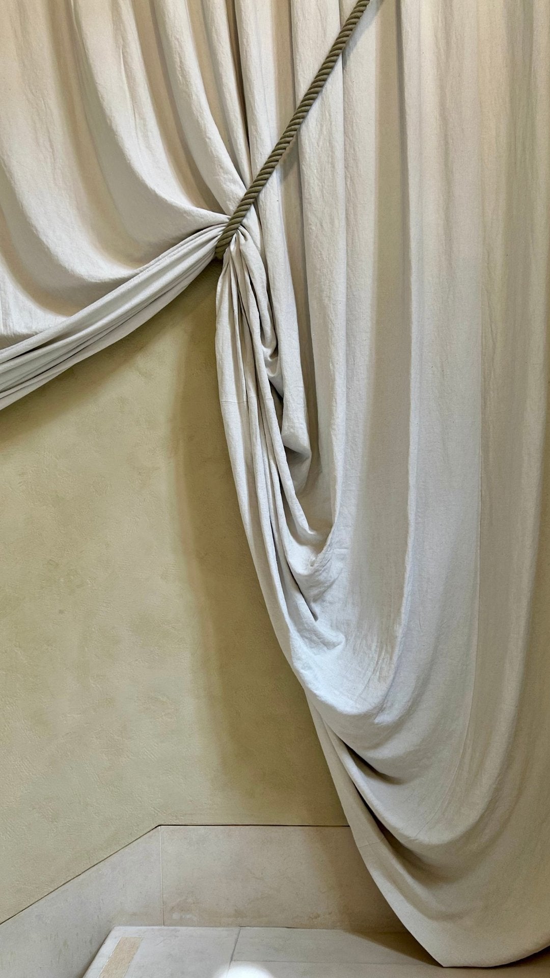 Heavy antique linen drawn back with a twisted cord, falling in soft folds to a stone floor