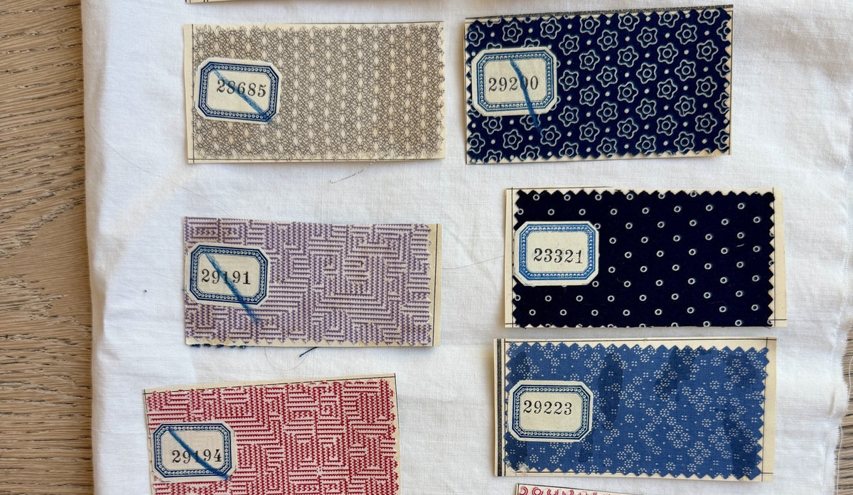 A sheet of numbered French mill print swatches with pinked edges and blue pencil marks, laid on white linen
